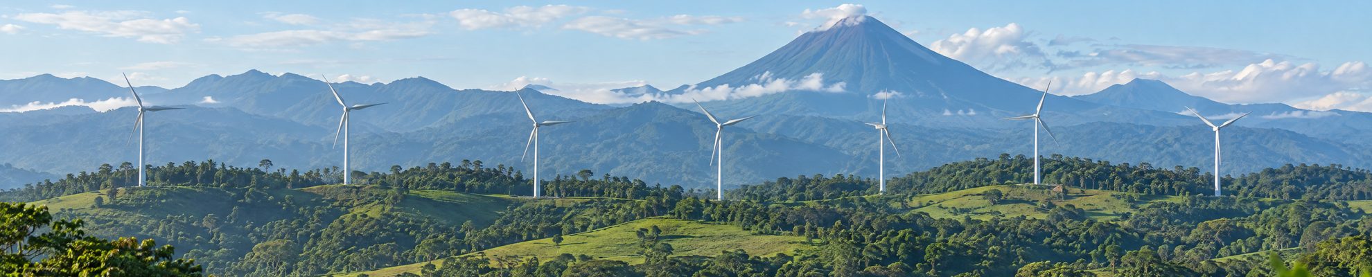 Aerogeneradores sobre cerros verdes en Costa Rica con un volcán al fondo, parte de la matriz eléctrica 98,6 por ciento renovable